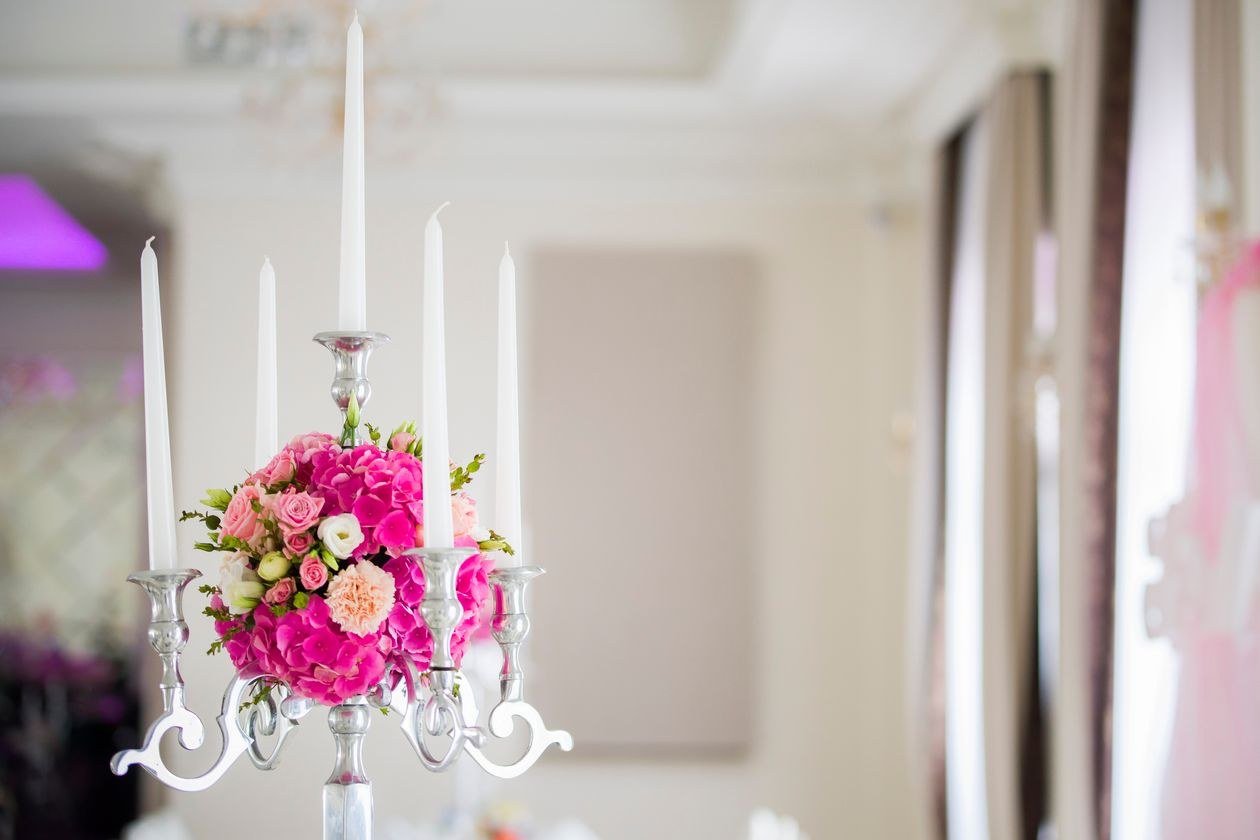 Elegant banquet table with white wax candles in metal candelabrum decorated with fresh flowers