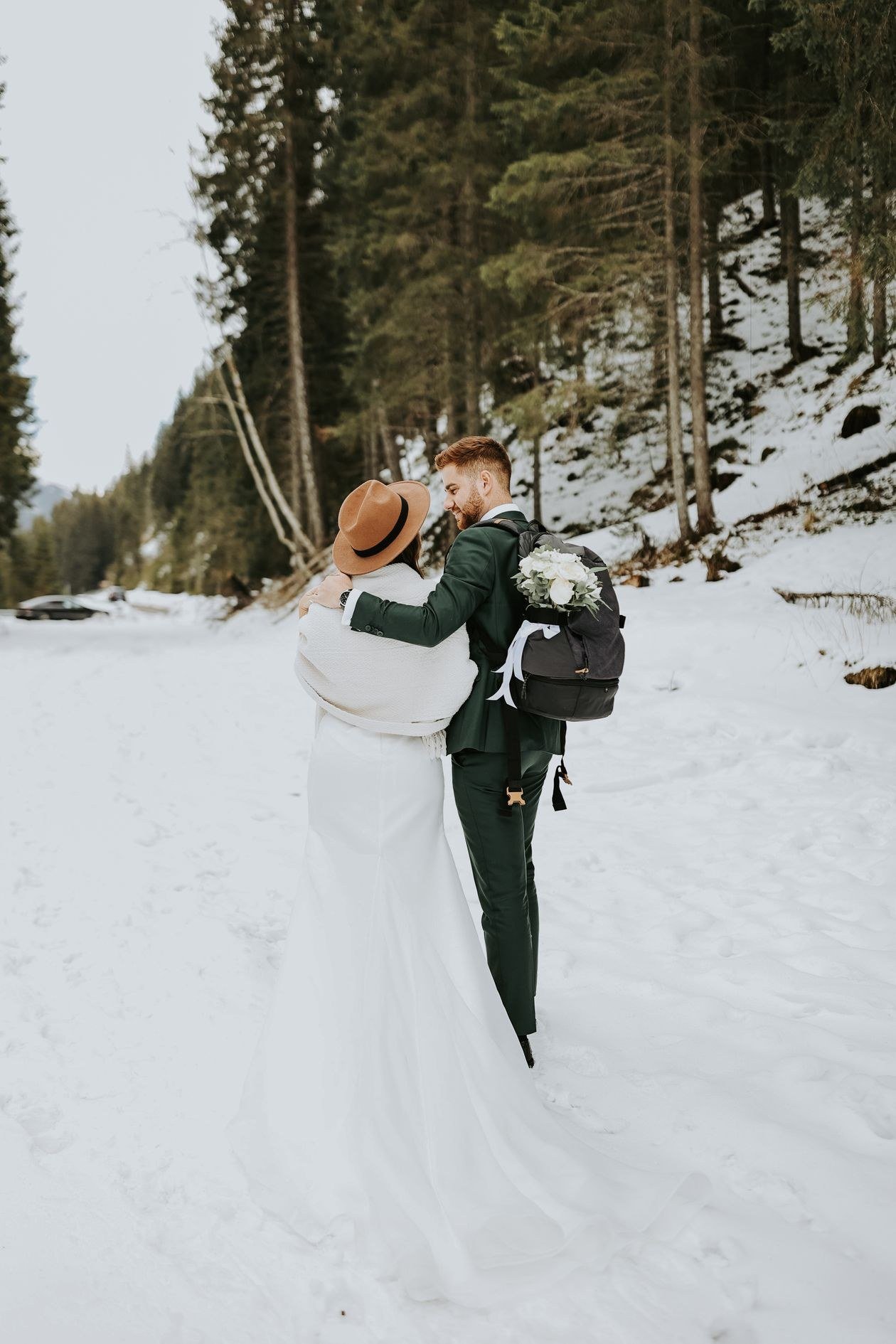 A loving couple in wedding attire embraces in a snowy forest setting, creating a magical winter scene