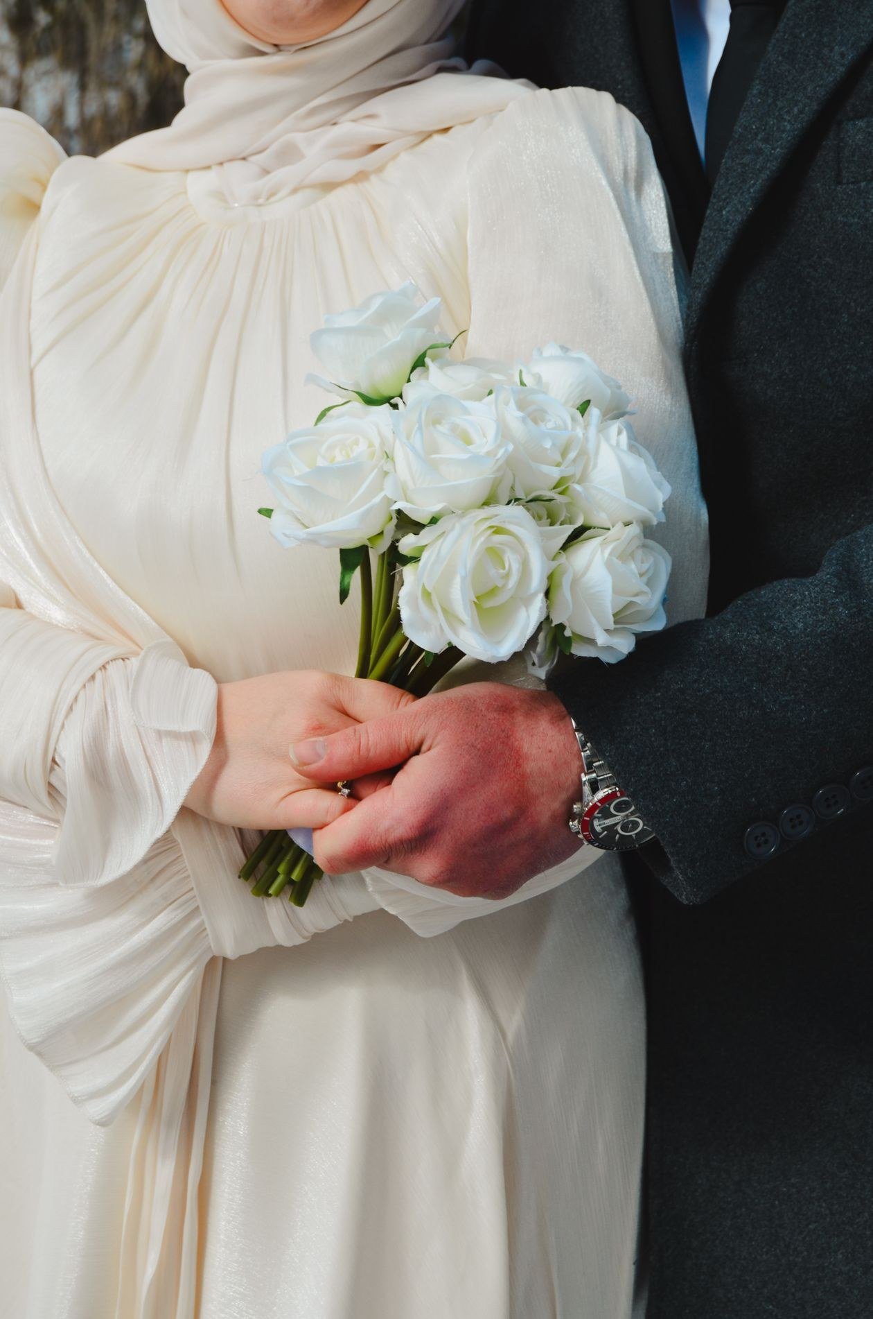Close-up of a couple in winter attire, embracing with white roses