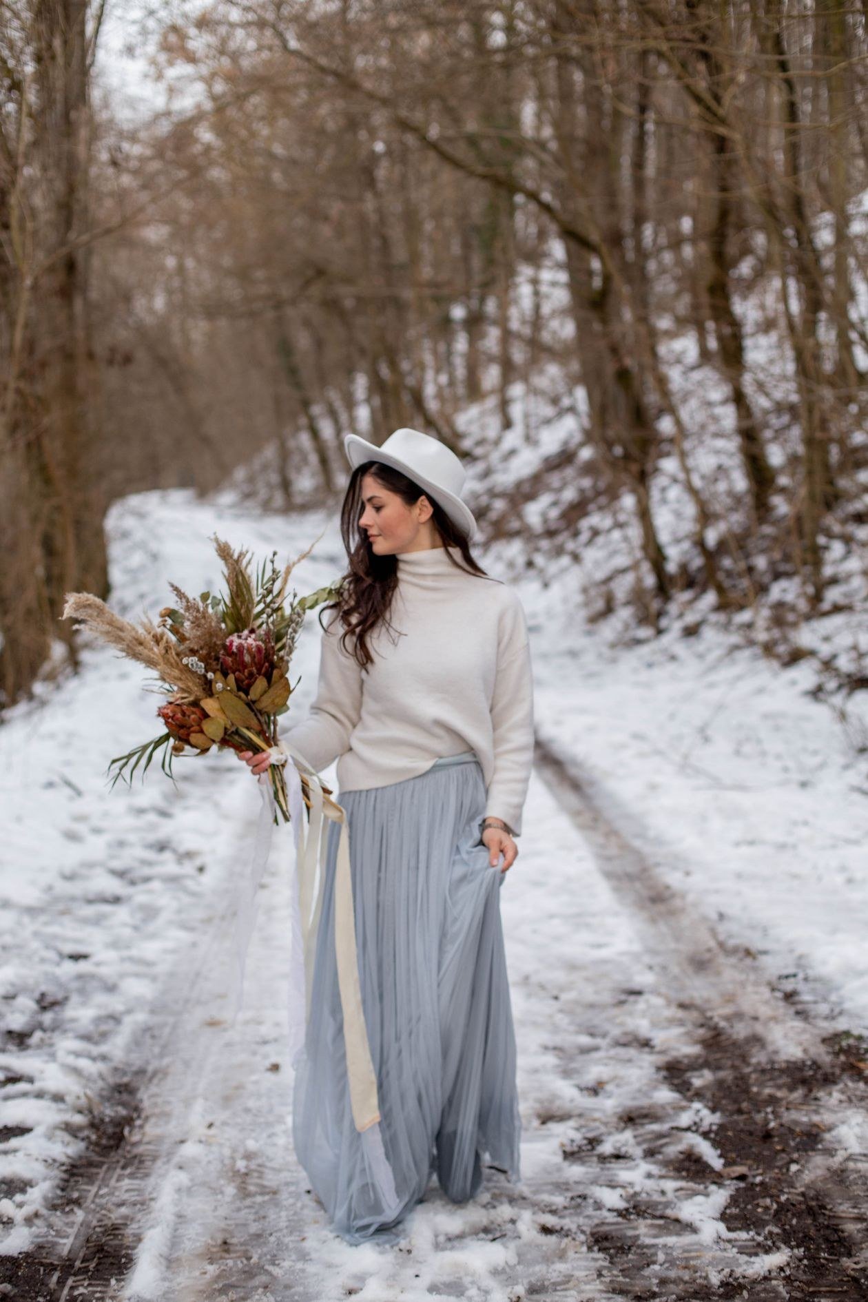 A bride with a bouquet walking along a snowy forest path, exuding elegance and grace