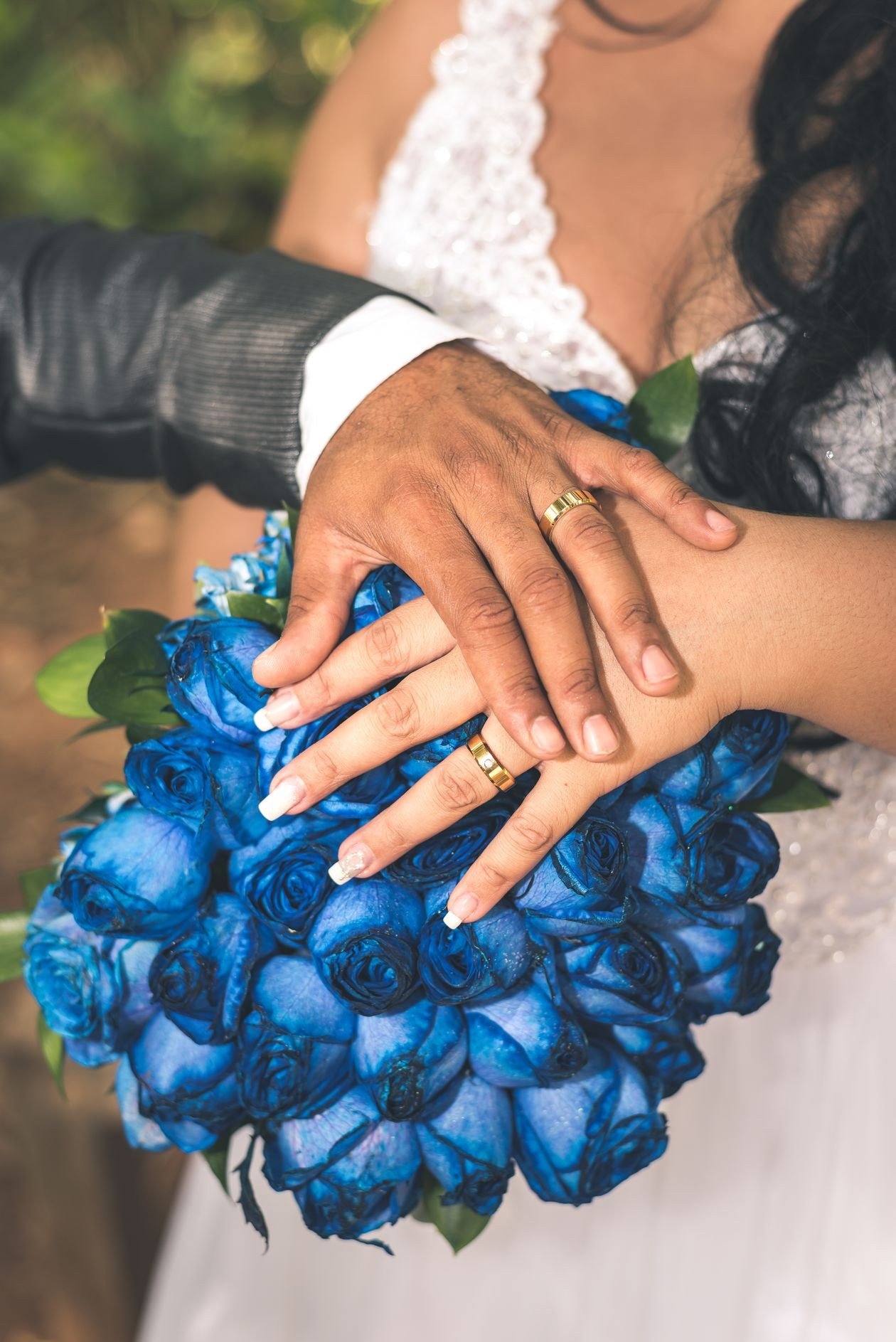 Close-up of newlyweds' hands on a blue rose bouquet, showcasing wedding rings