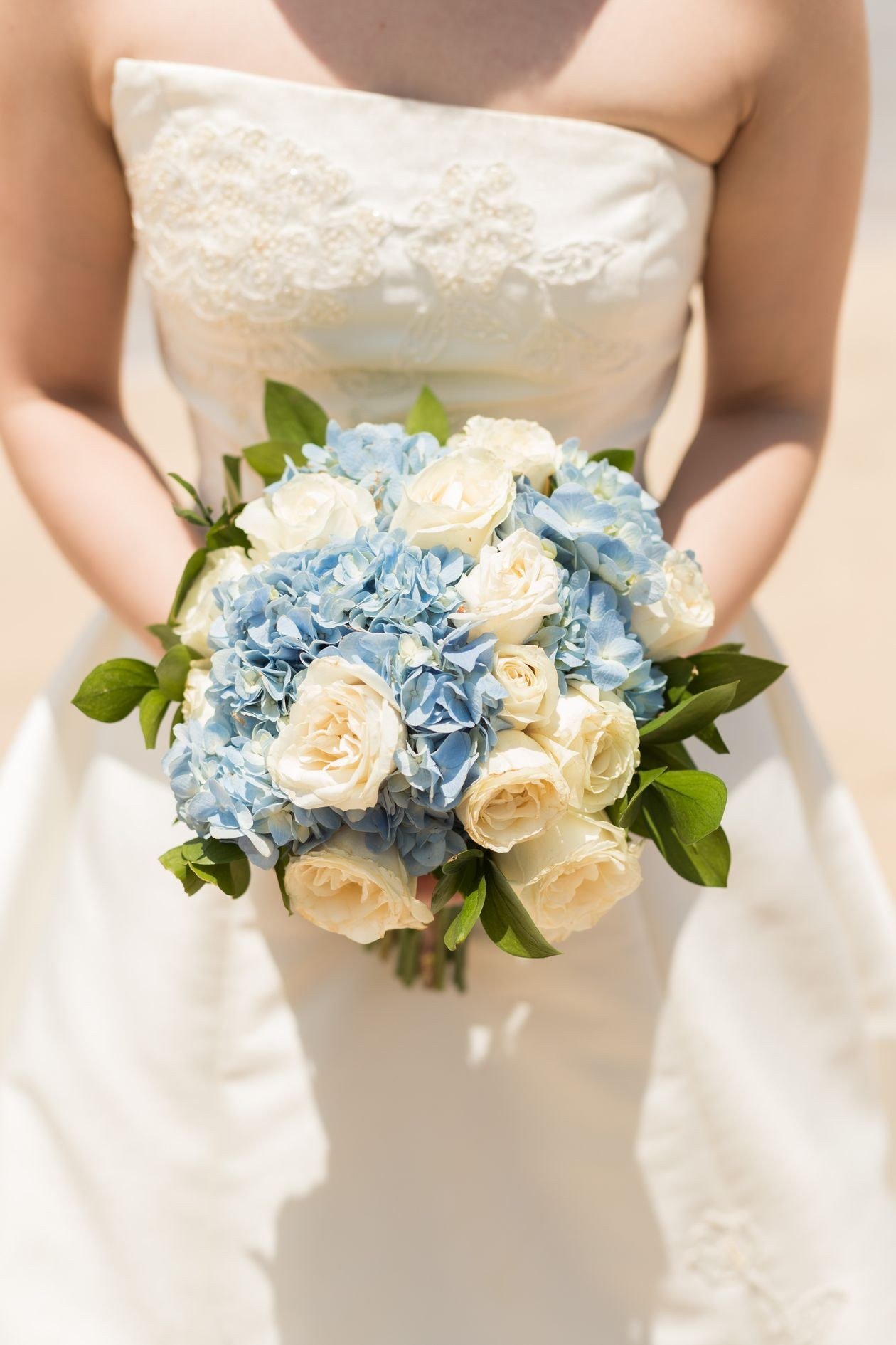 Bride in white dress holding a bouquet of blue hydrangeas and white roses