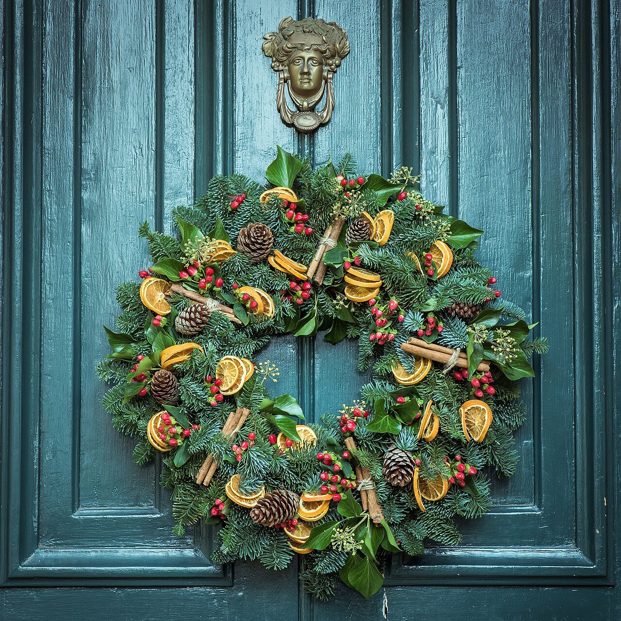 Autumn wreath with pinecones and dried oranges on a teal door