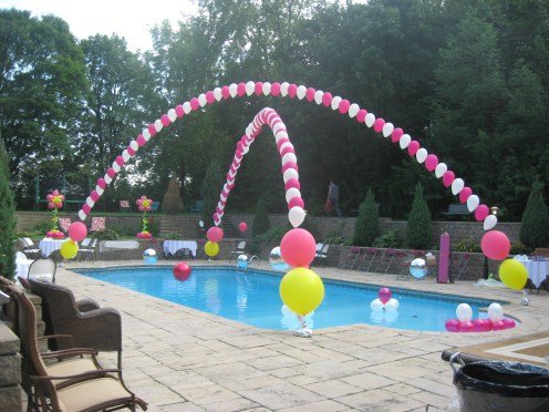 Pink and white balloon arch over a pool