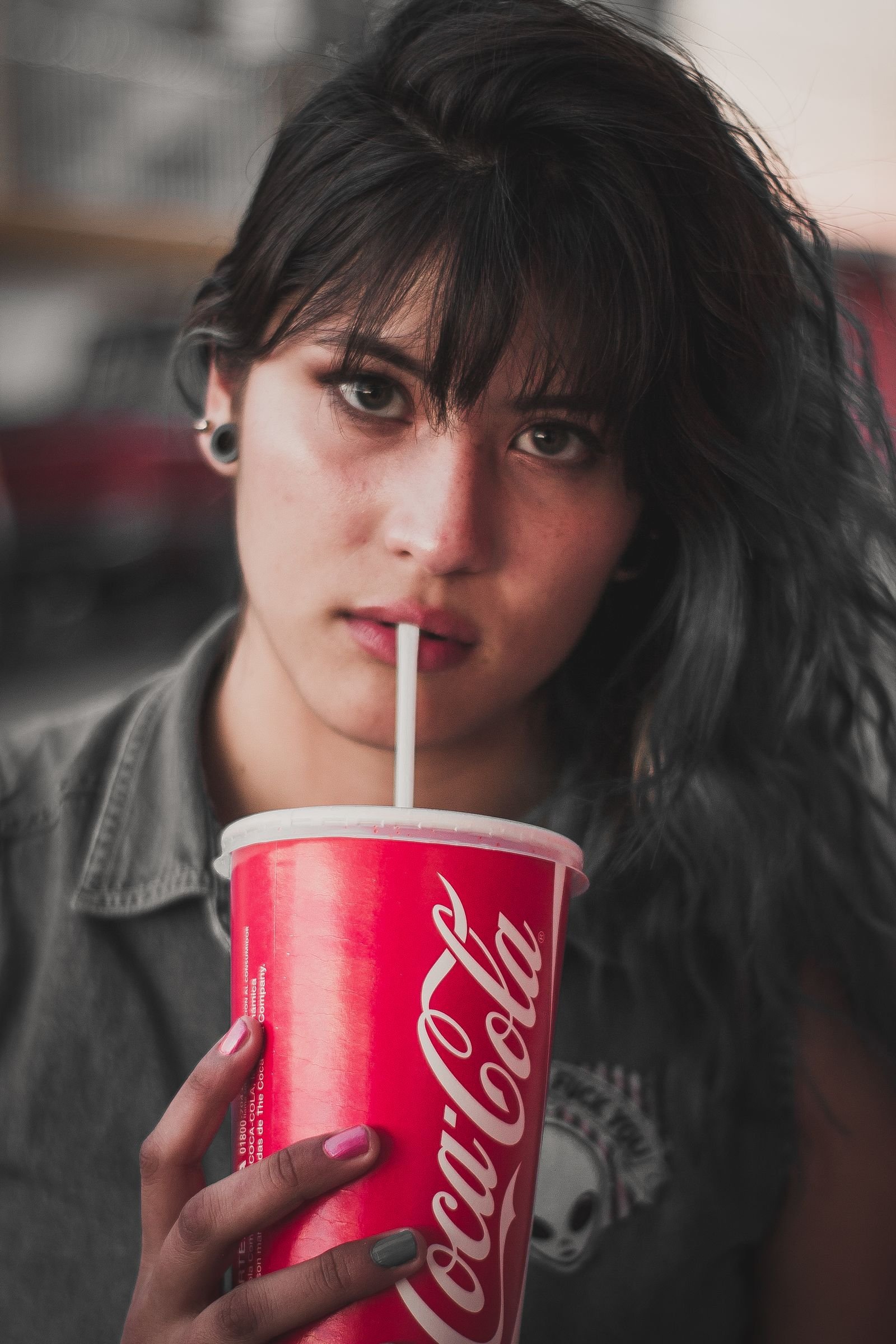 Young woman with wavy cherry cola hair sipping Coca-Cola through a straw
