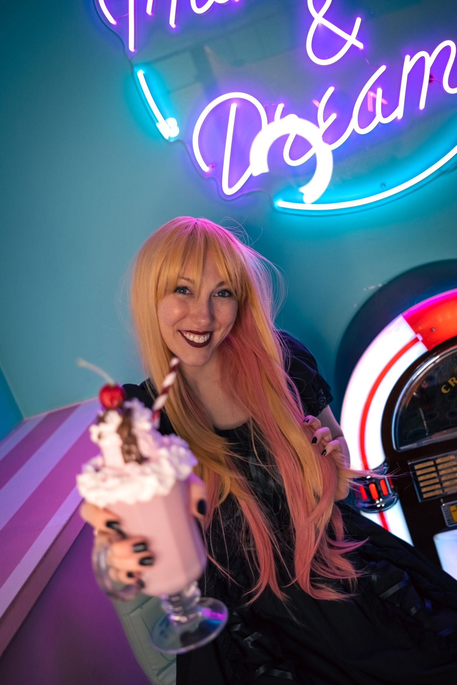 Woman with colourful red hair holding a milkshake in a neon-lit diner