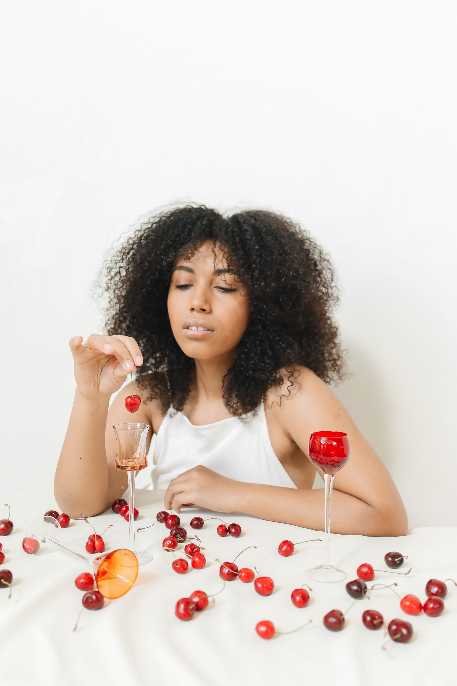 Woman savouring cherry cocktails surrounded by fresh cherries and glassware