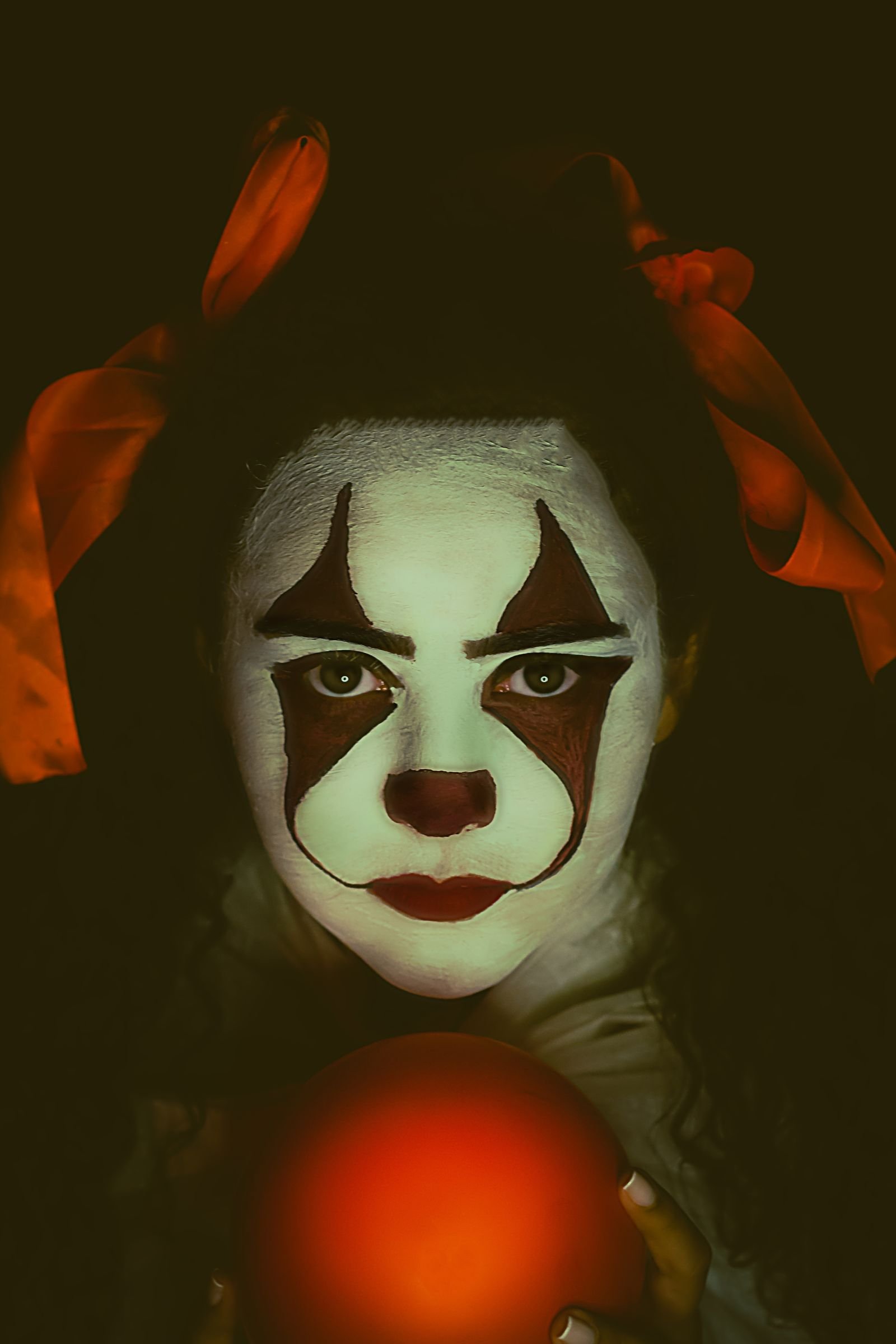 Mysterious clown holding a red ball at a Halloween carnival party
