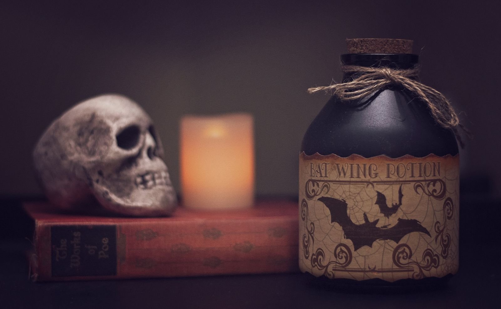 Spooky still life featuring a skull, bat potion bottle, candle and book