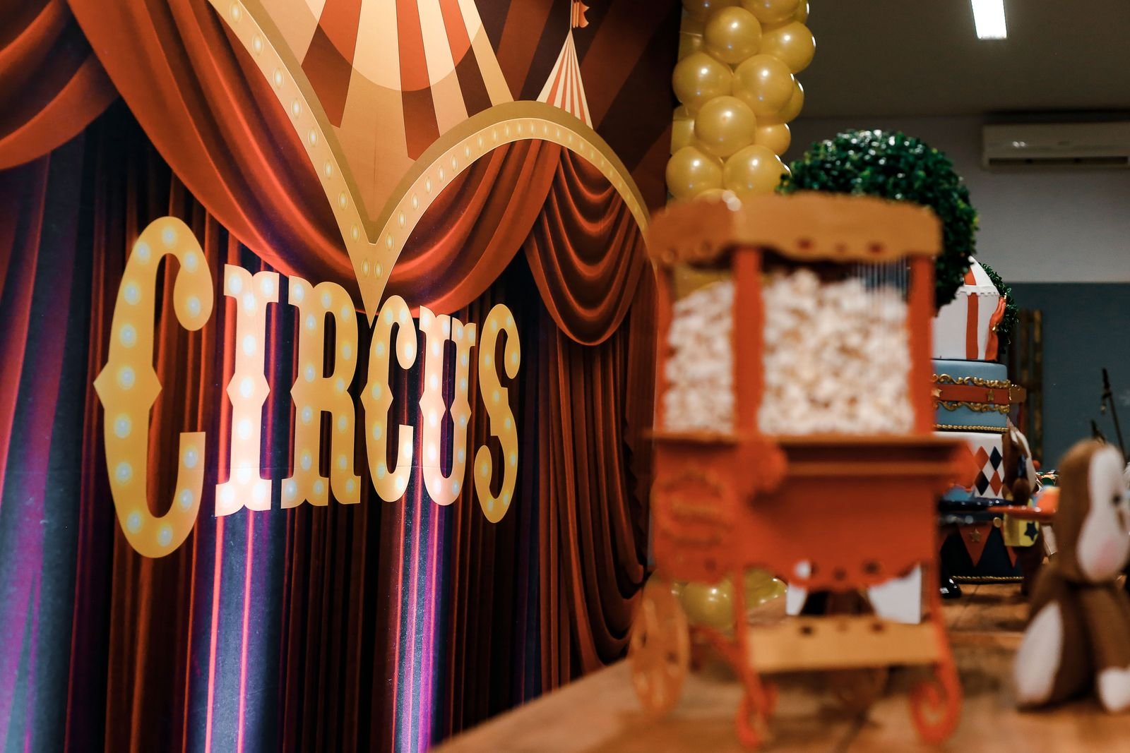 Colourful circus-themed party decorations featuring popcorn cart and balloons indoors