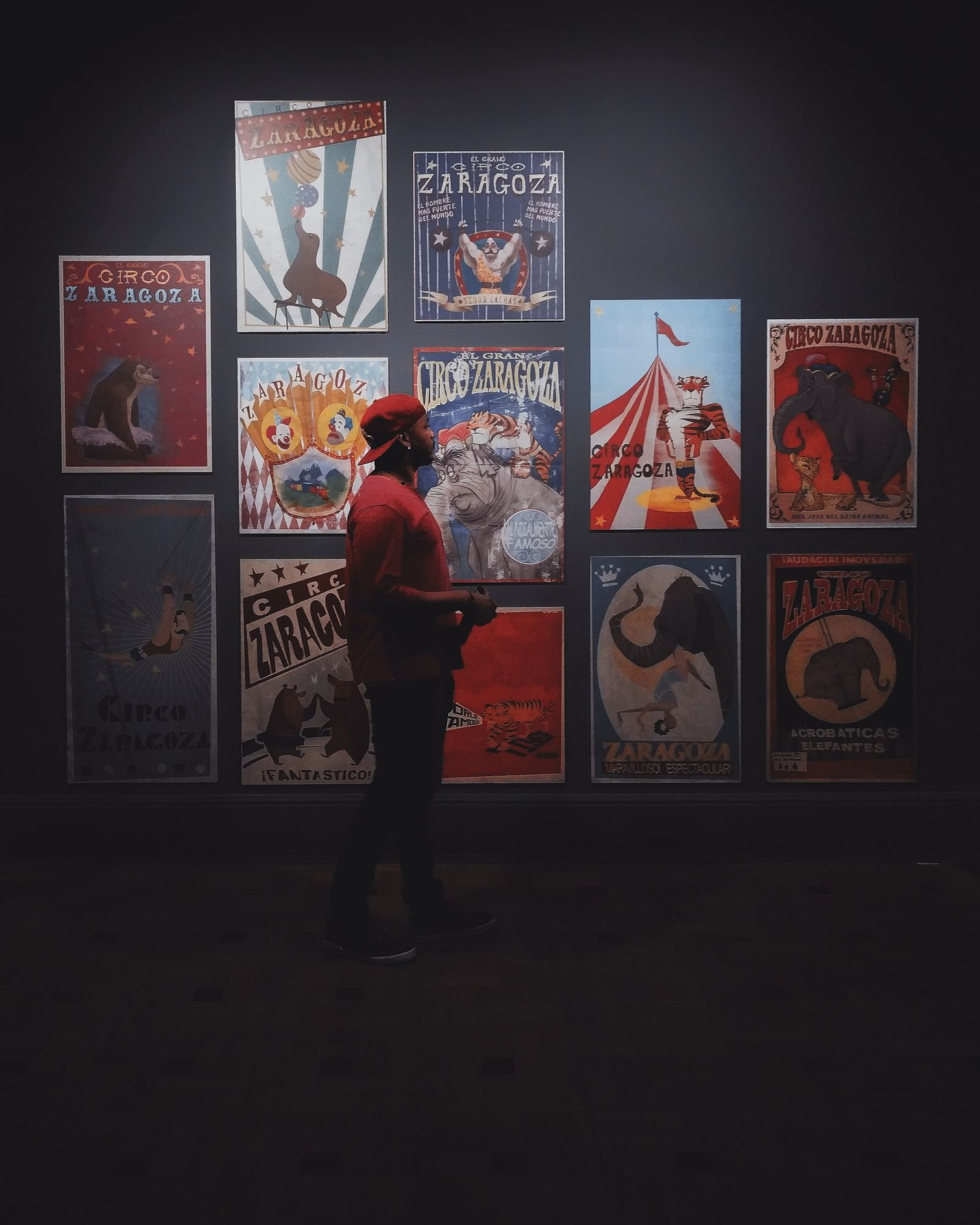 Man in red cap observing colourful vintage circus posters indoors