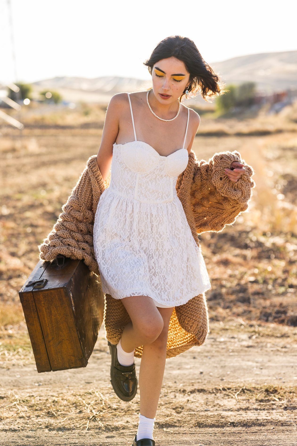 Woman in white lace mini dress carrying vintage suitcase