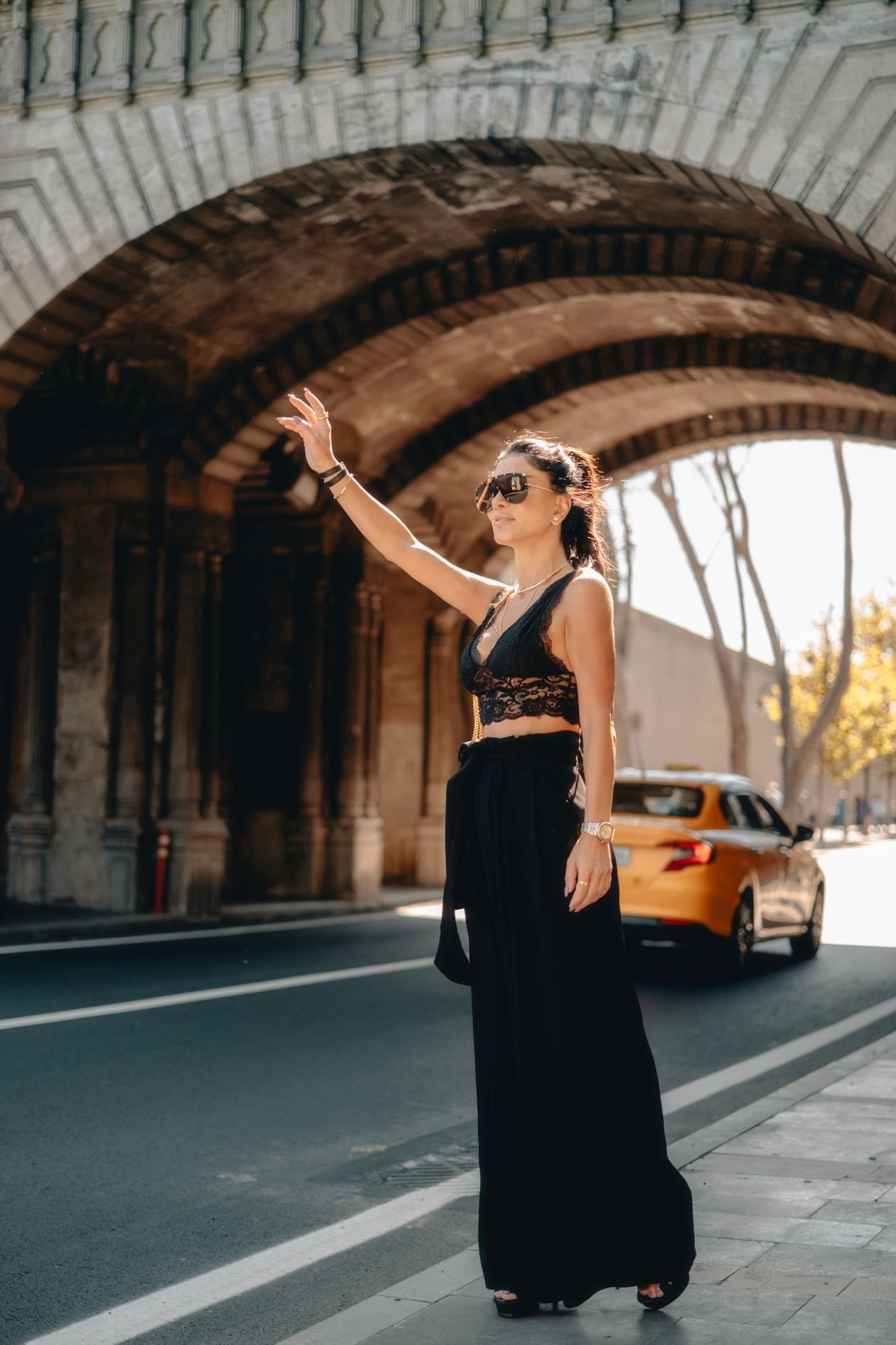 Model in black lace crop top and palazzo pants hailing a taxi