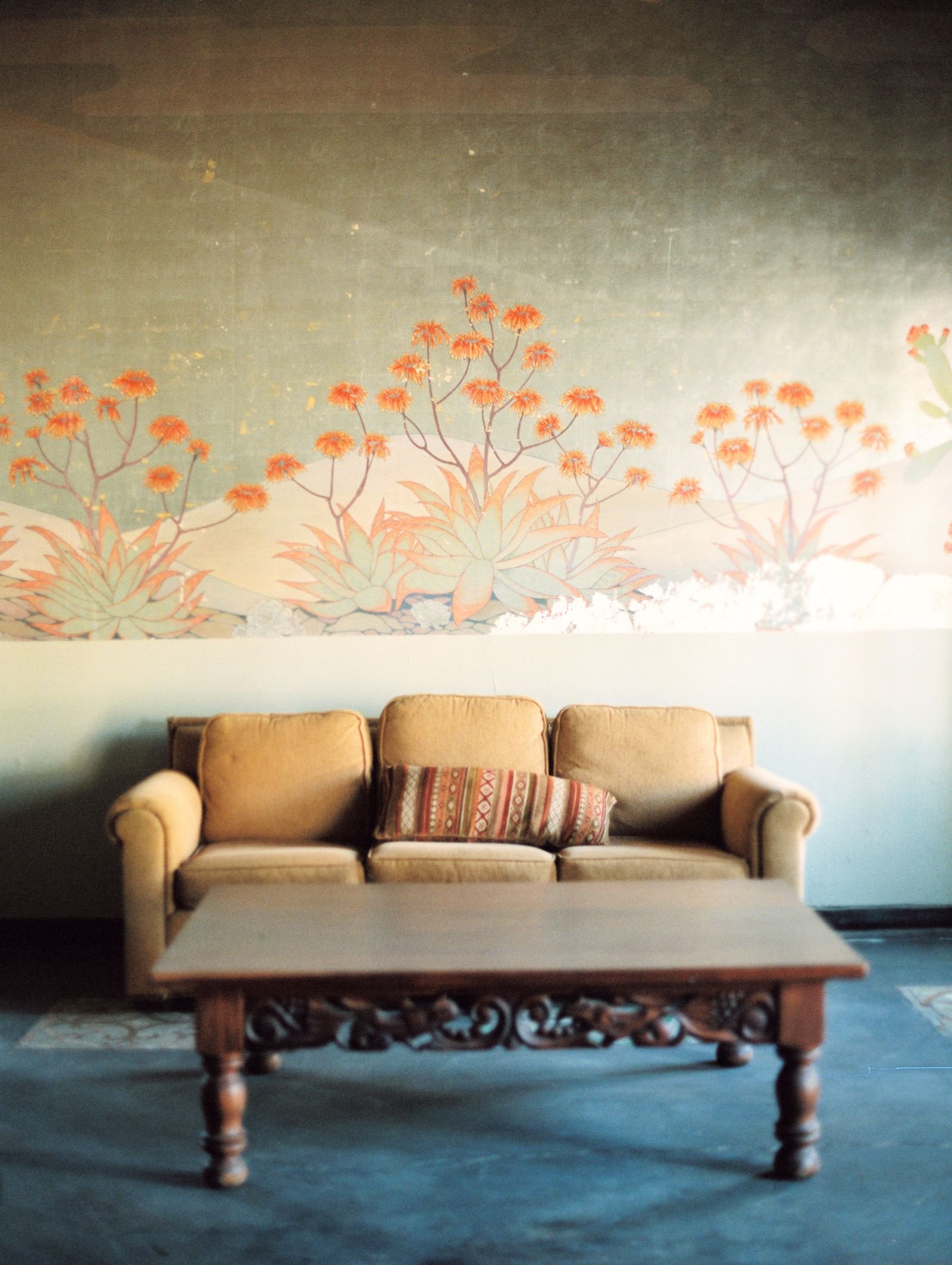 Elegant minimalist living room with vintage couch, wooden table, and artistic floral wall design