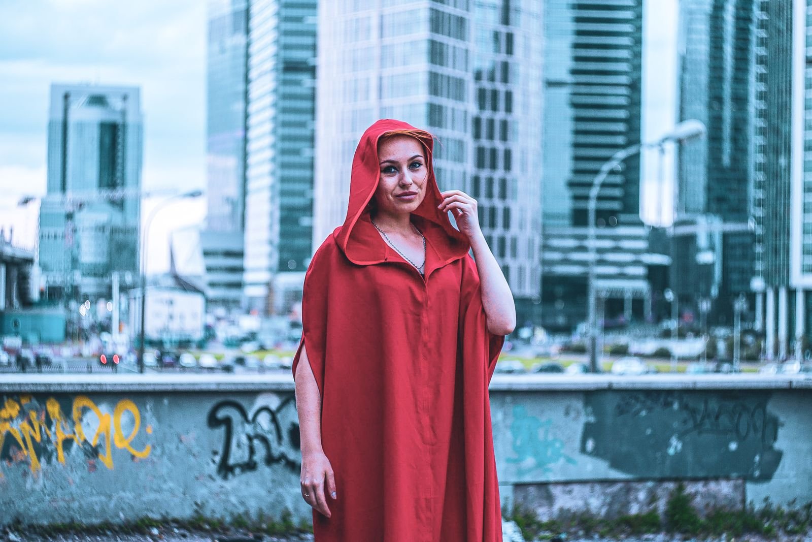 Woman in red cloak against modern cityscape fashion mystery