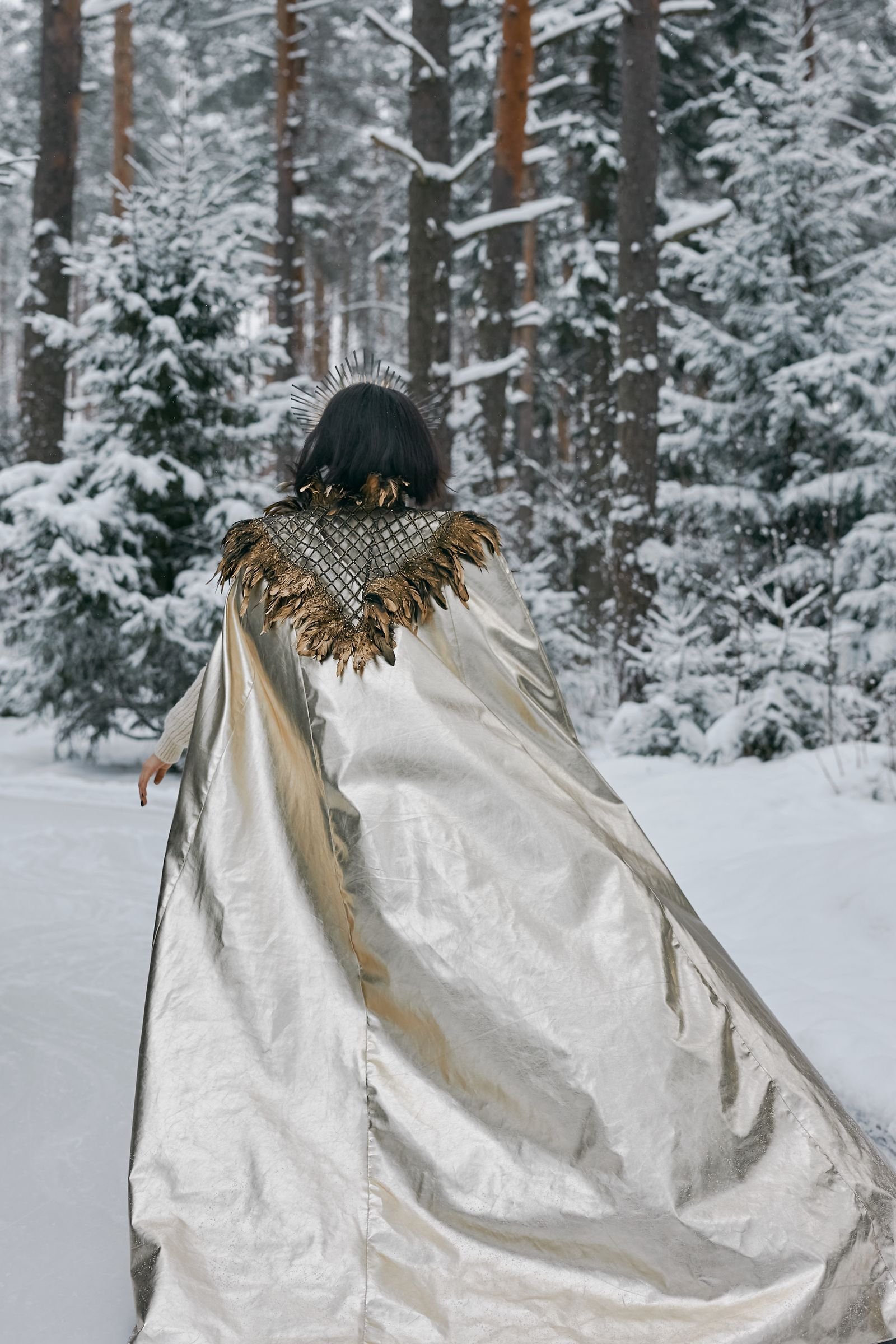 Woman in silver cape walking through serene snowy forest