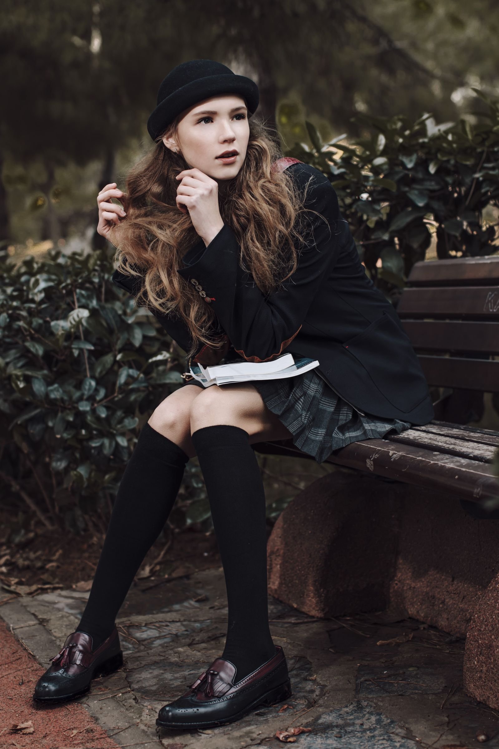 Young woman in pleated uniform skirt and blazer with books on a park bench