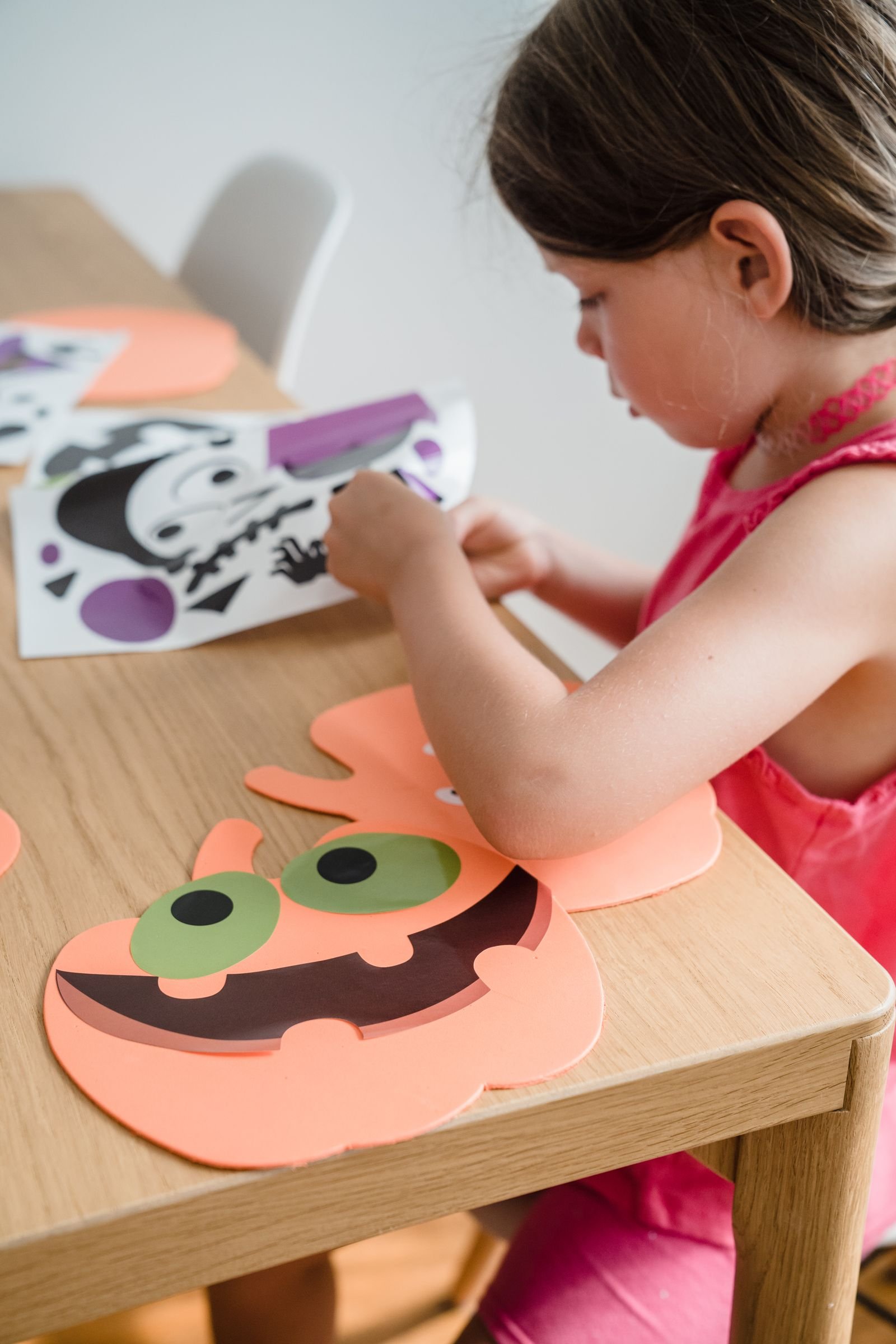 Young girl assembling orange paper pumpkin decorations at a table indoors
