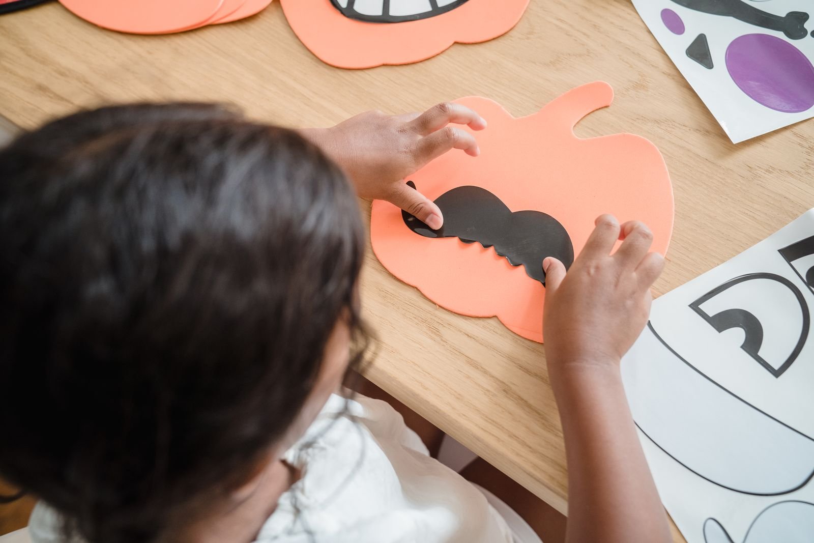 Child assembling 3D paper pumpkins from orange card for Halloween centrepieces