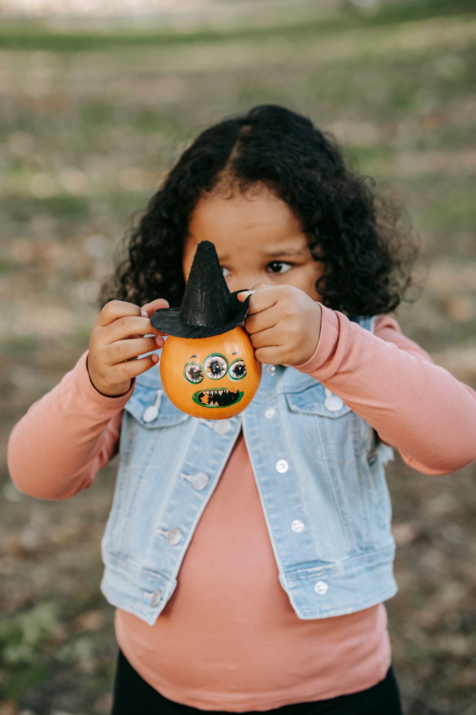 Little girl in casual clothes playing with a small painted Halloween pumpkin
