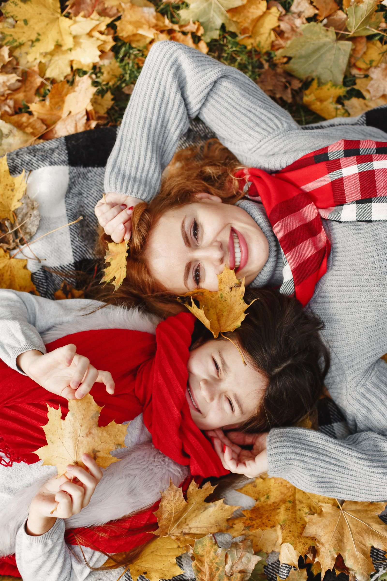 Mother and daughter smiling together in autumn leaves wearing red scarves