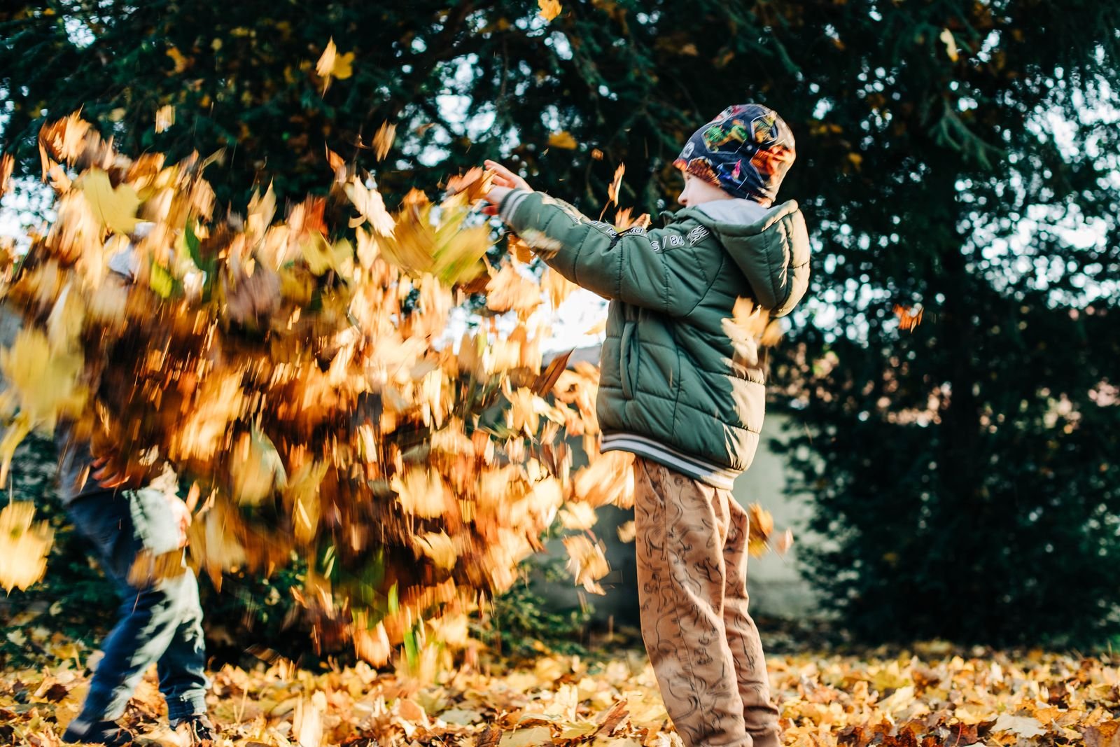 Two children joyfully playing with leaves in a sunlit autumn park