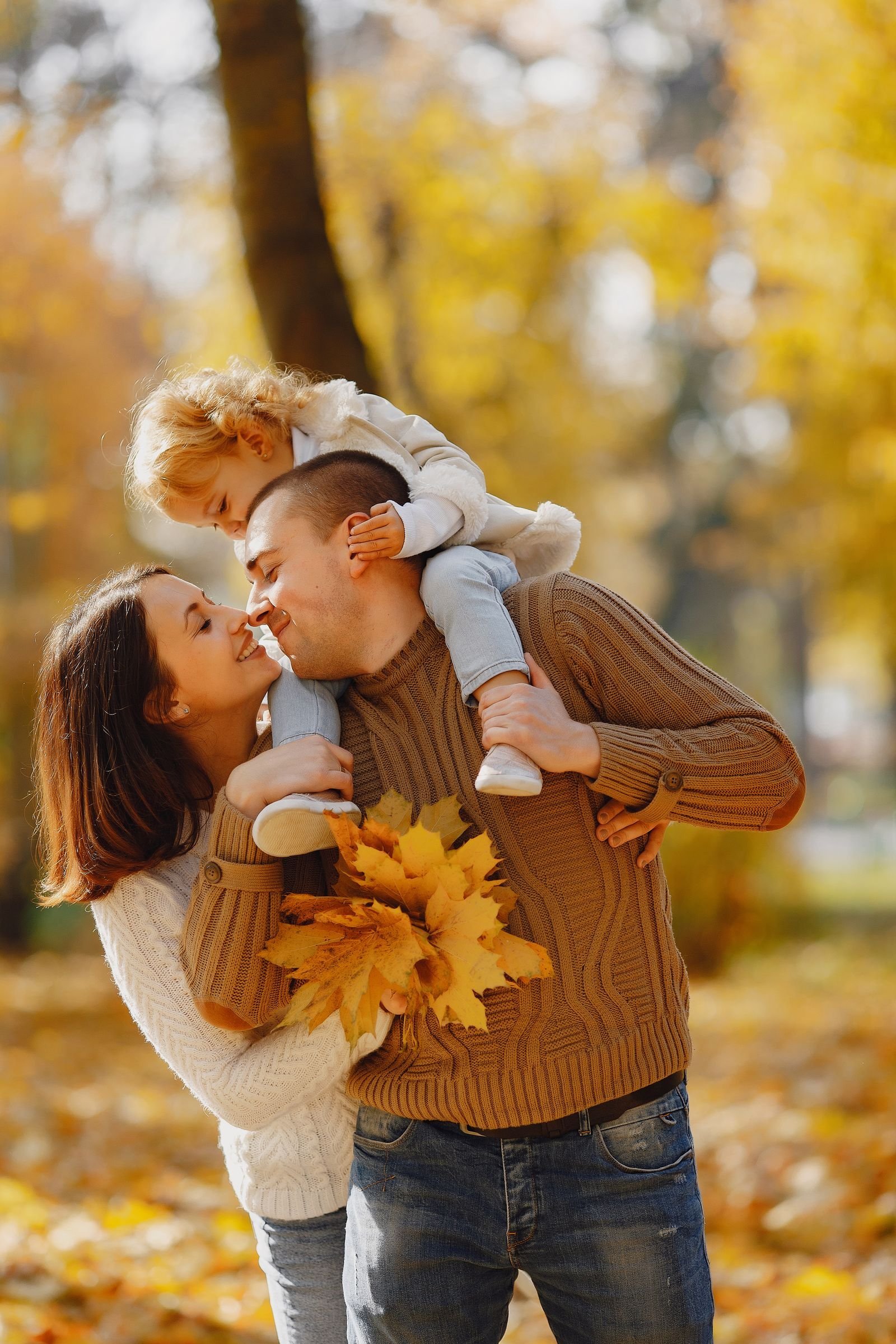 Father carrying little daughter on shoulders collecting maple leaves with mother