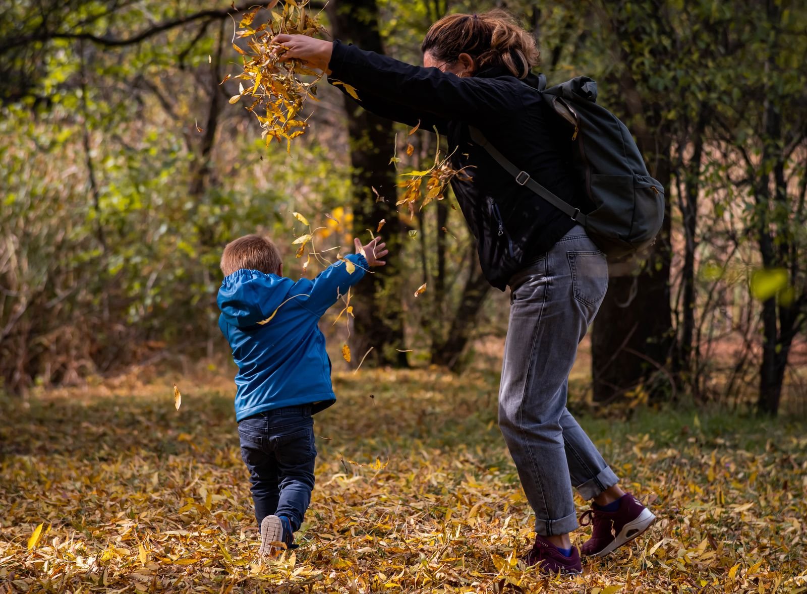 Mother and child playing with leaves together in an autumn forest setting
