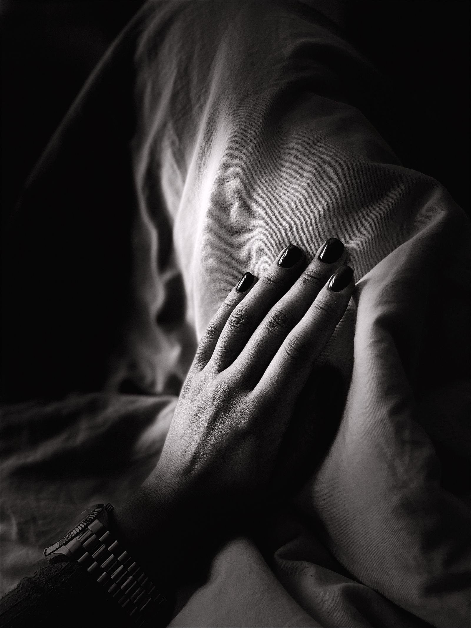 Monochrome close-up of painted nails resting on soft dark fabric