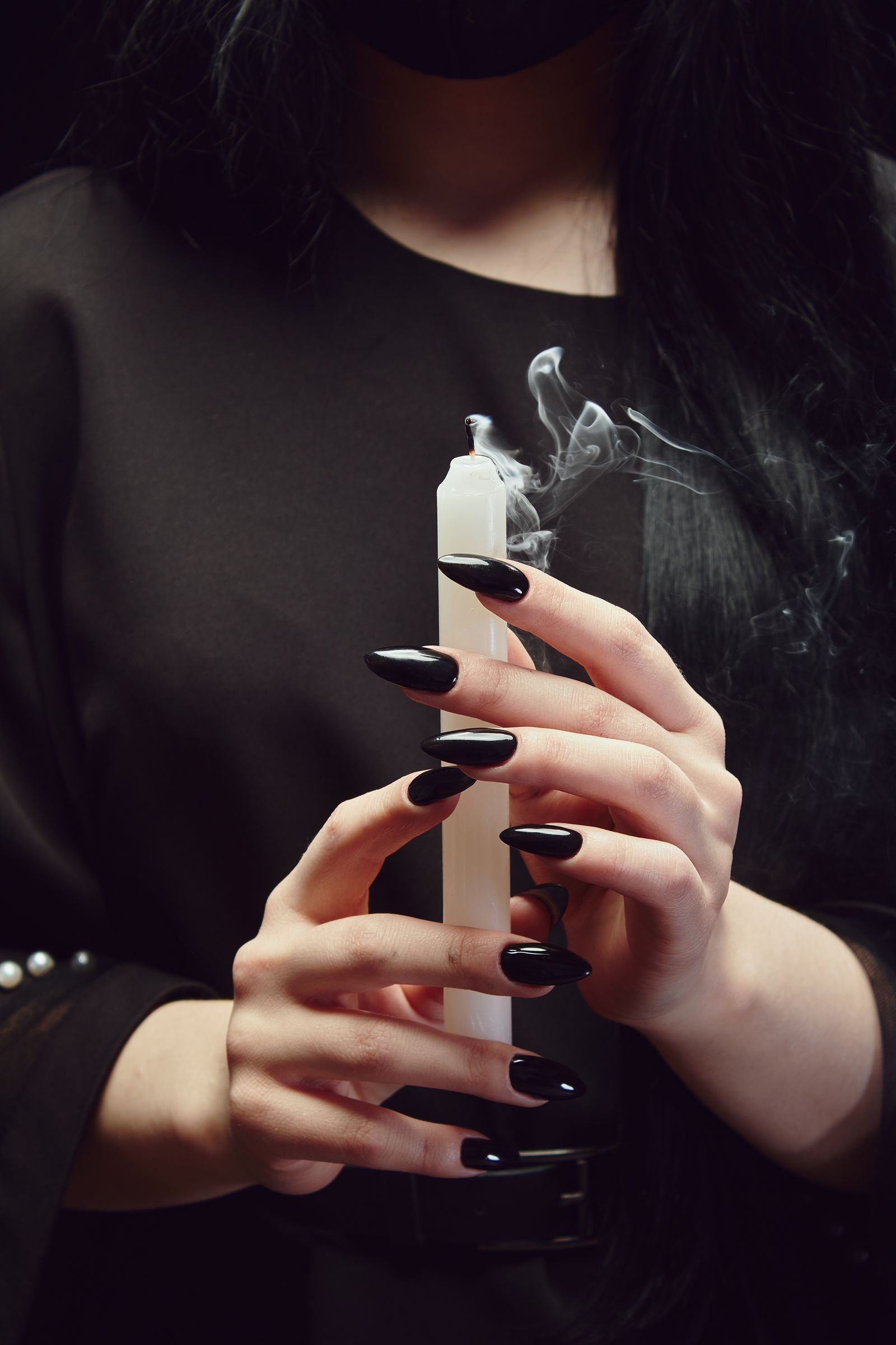 Black polished nails holding a white candle in mysterious ambiance