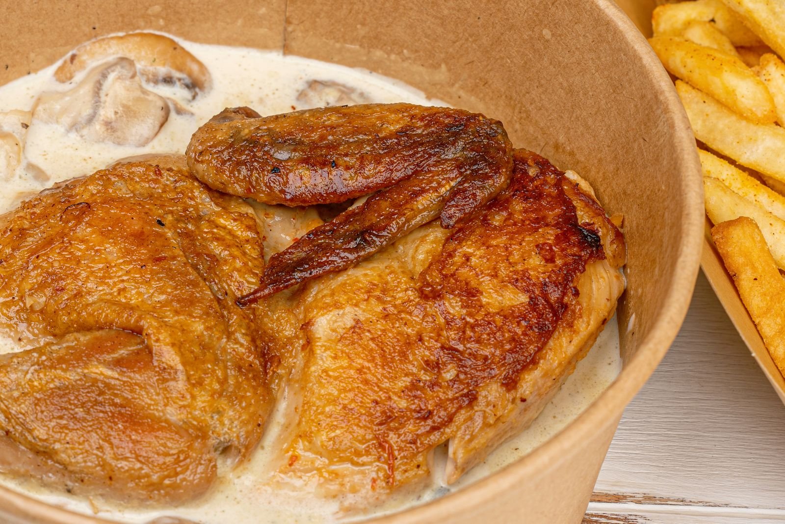 Roasted chicken with mushroom sauce in paper bowl served with fries