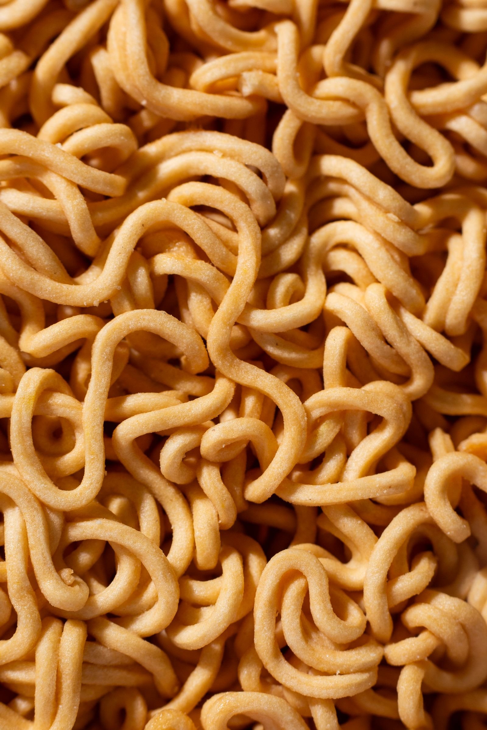 Long noodles lifted from a bowl with tongs, steam rising