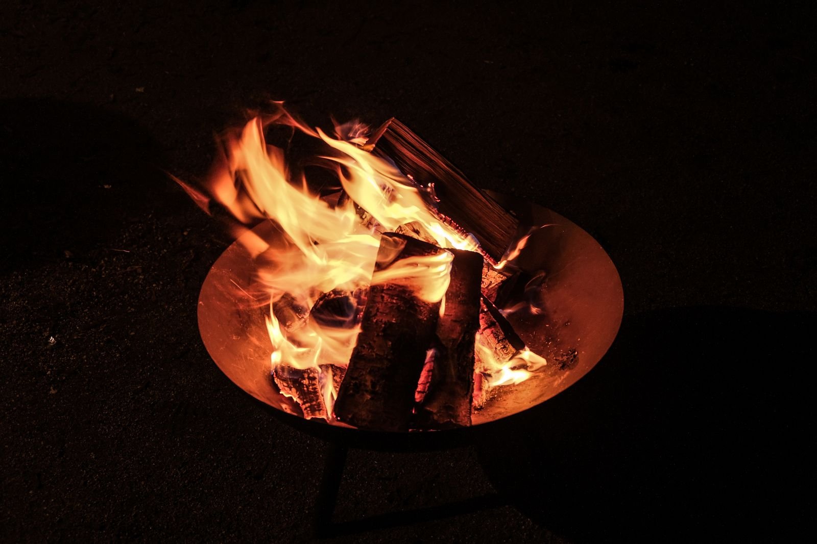 A round metal fire pit with flames on a patio at night