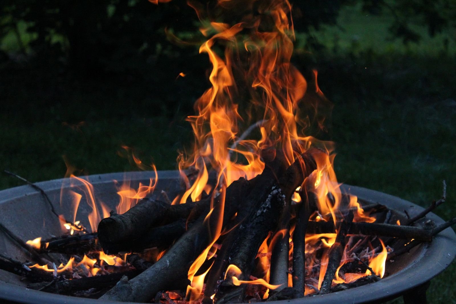 A bonfire flickering in a fire pit outdoors at dusk