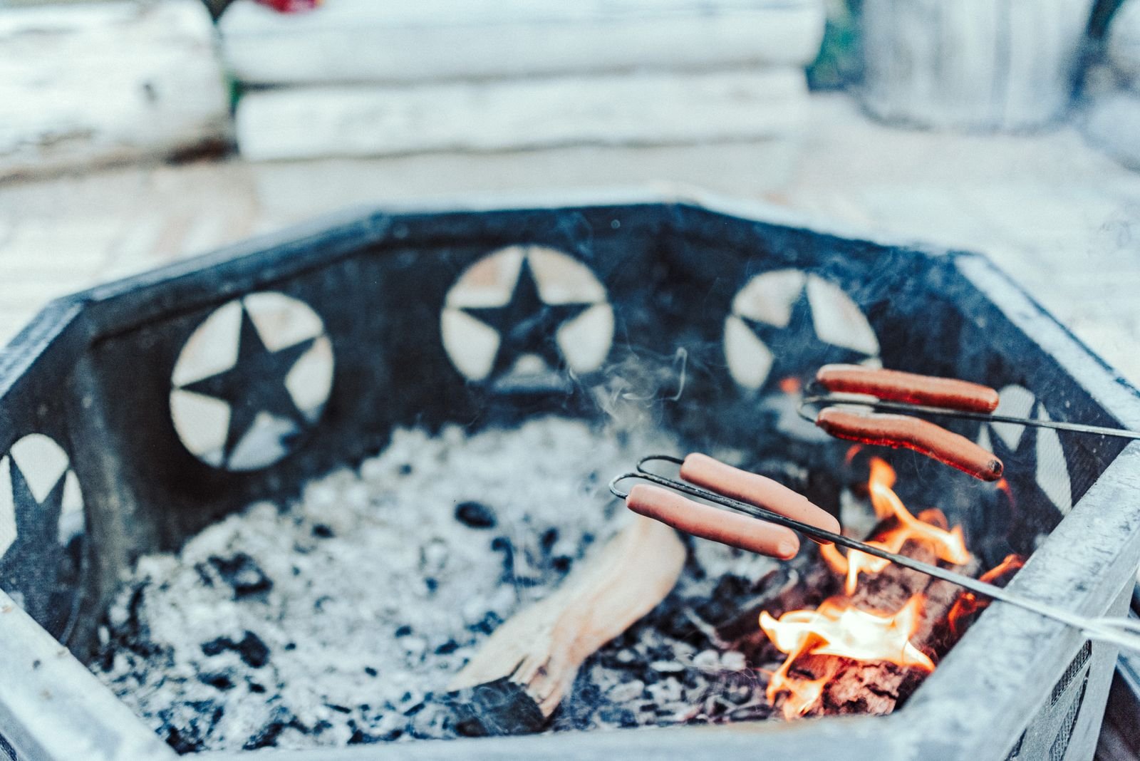 Hot dogs roasting on sticks over a rustic fire pit