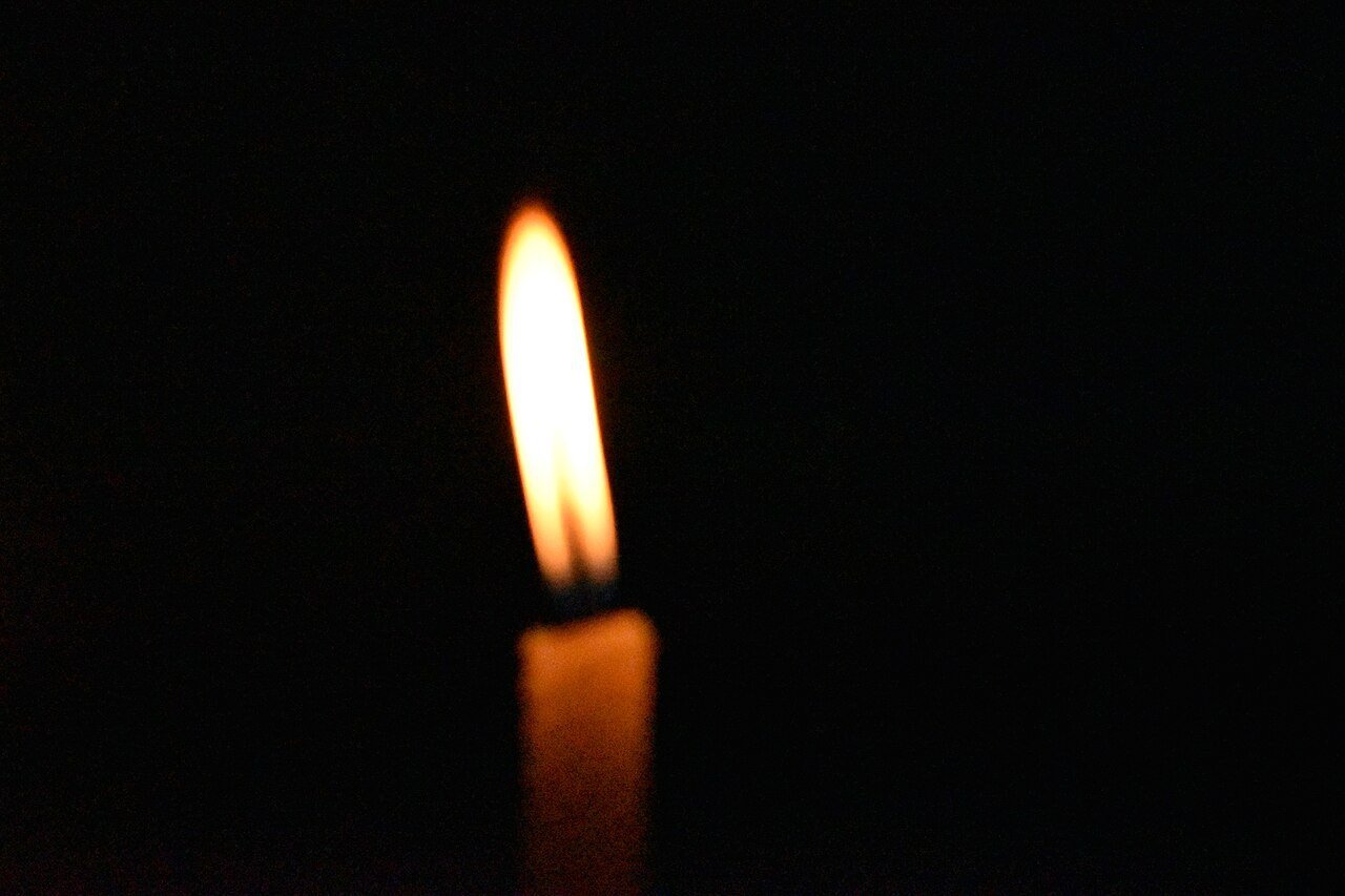 A single candle flame glowing against a black background