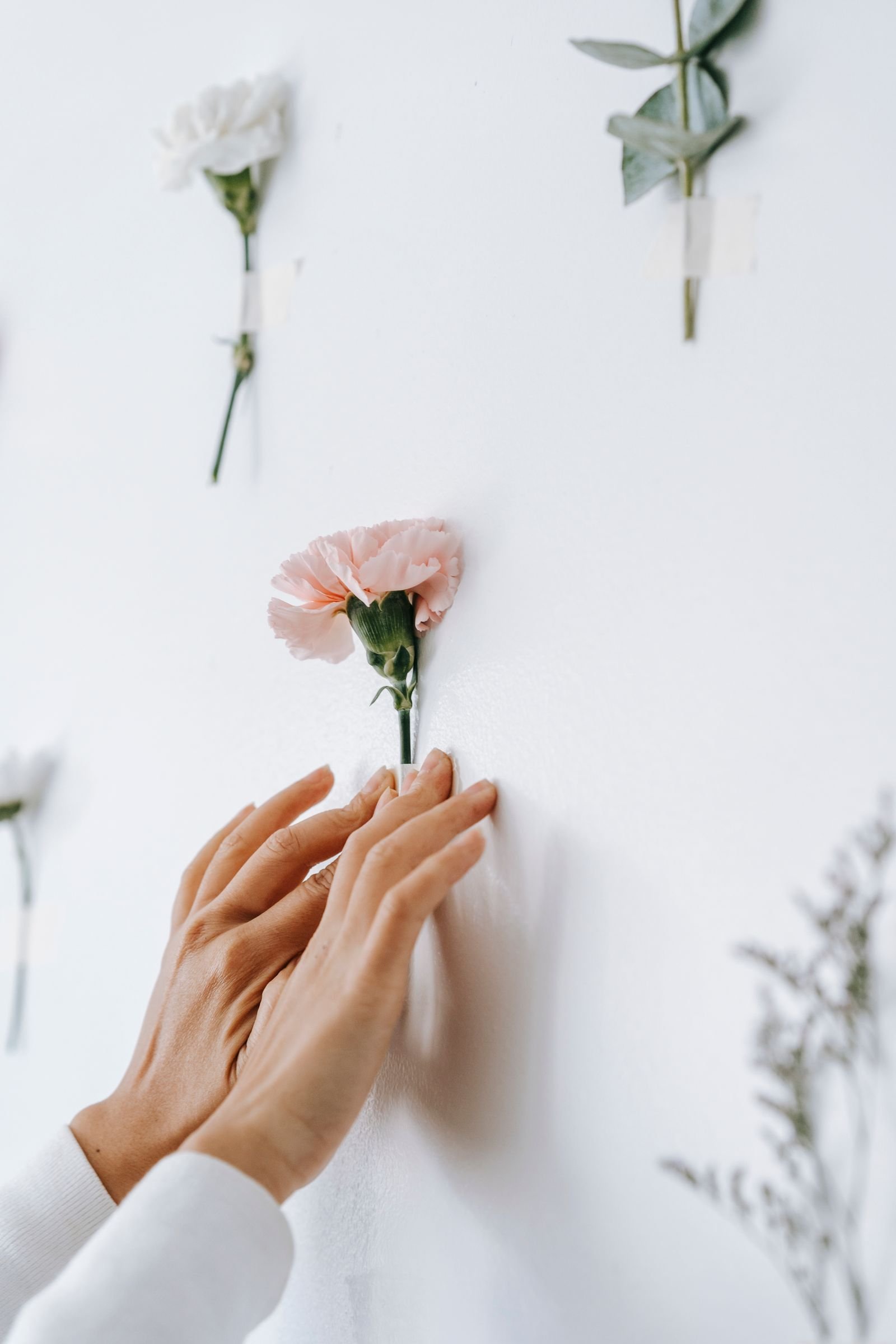 Hands arranging delicate flowers for a DIY botanical wall display